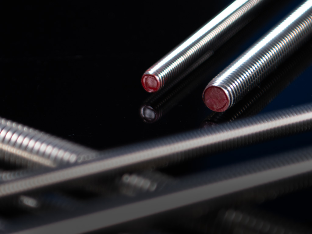 Nahaufnahme von zwei Edelstahl-Gewindestangen mit roten Endkappen, glänzende Oberfläche und klar erkennbare Gewindegänge auf schwarzem Untergrund