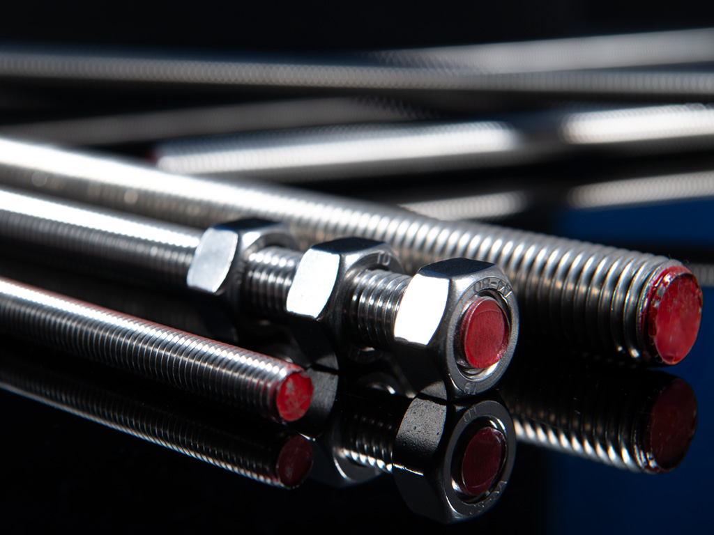 Edelstahl-Gewindestangen mit roten Endkappen und aufgeschraubten Muttern auf schwarzem Hintergrund, glänzend poliert und präzise gefertigt